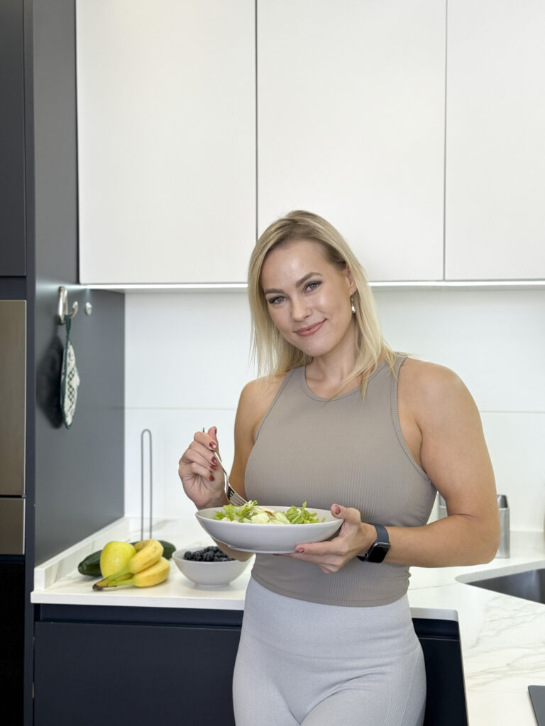 Naine, kes on personaaltreener, seisab moodsas köögis, käes salatikaussi ja kahvlit, naeratab kaamerasse. Banaanid, pirnid ja mustikad seisavad tema taga leti peal. Ta kannab varrukateta toppi ja kergeid sääriseid.